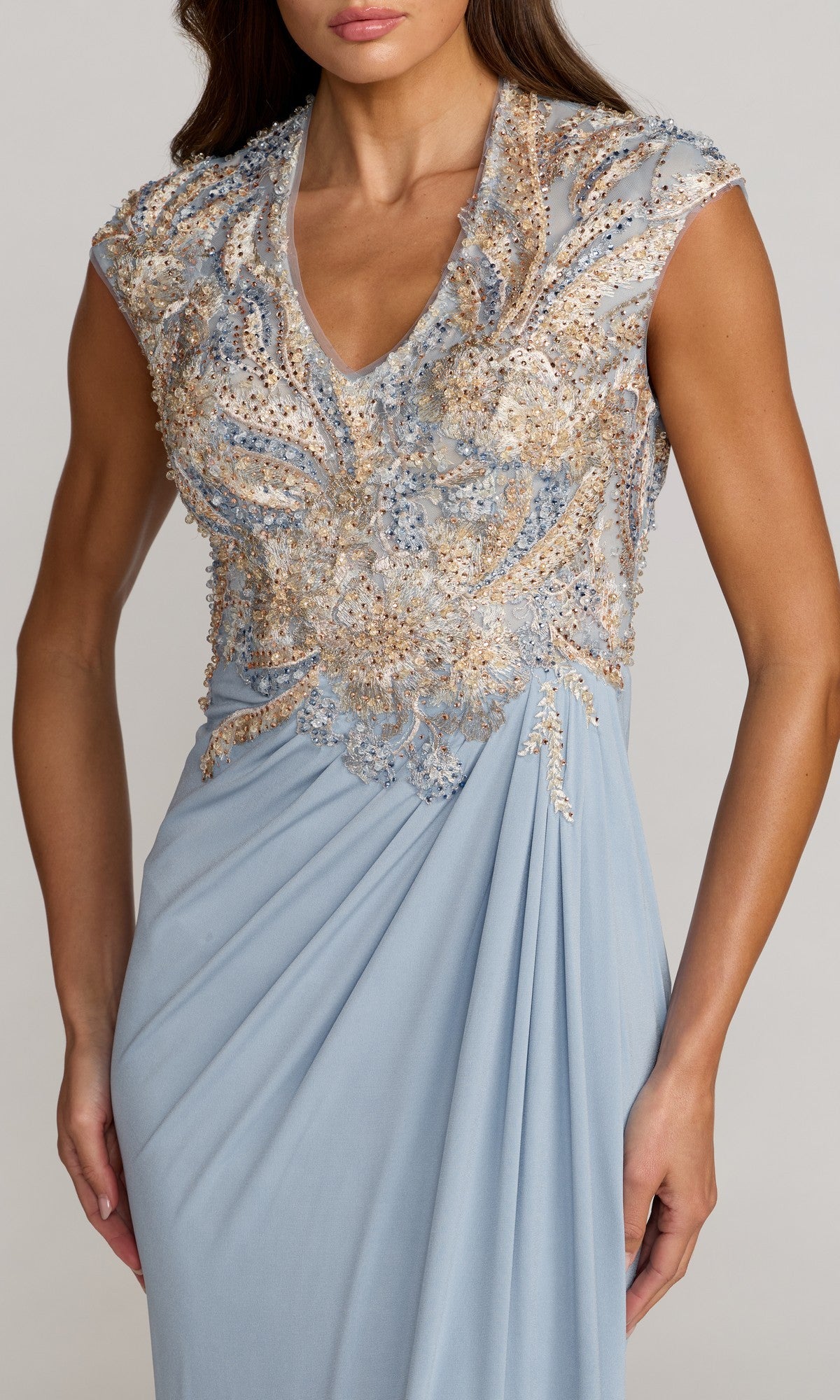 A woman wearing the Mac Duggal 21330 Long Formal Dress—a light blue evening gown with a v-neckline, an embroidered bodice embellished with gold and silver sequins, cap sleeves, and draped fabric detailing at the waist.